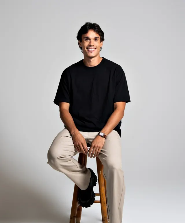 Lipe sorrindo, sentado num banco alto de madeira